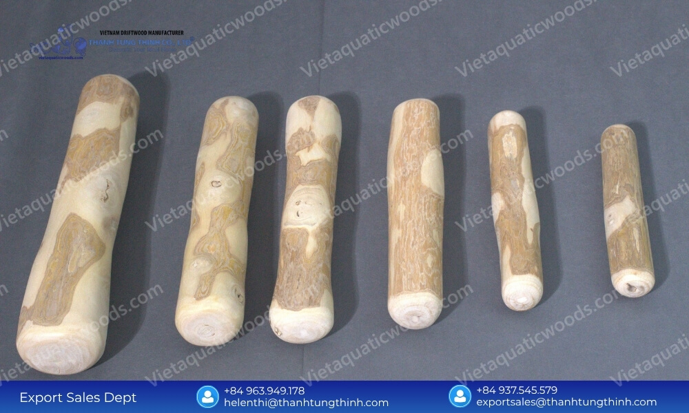 A row of six smooth mechanically sanded coffee wood dog chew vietnam sticks arranged from largest to smallest on a dark gray surface