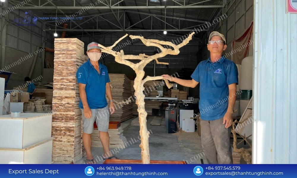 Two factory workers proudly displaying a giant custom coffee wood bird perch tree stand in the manufacturing hub