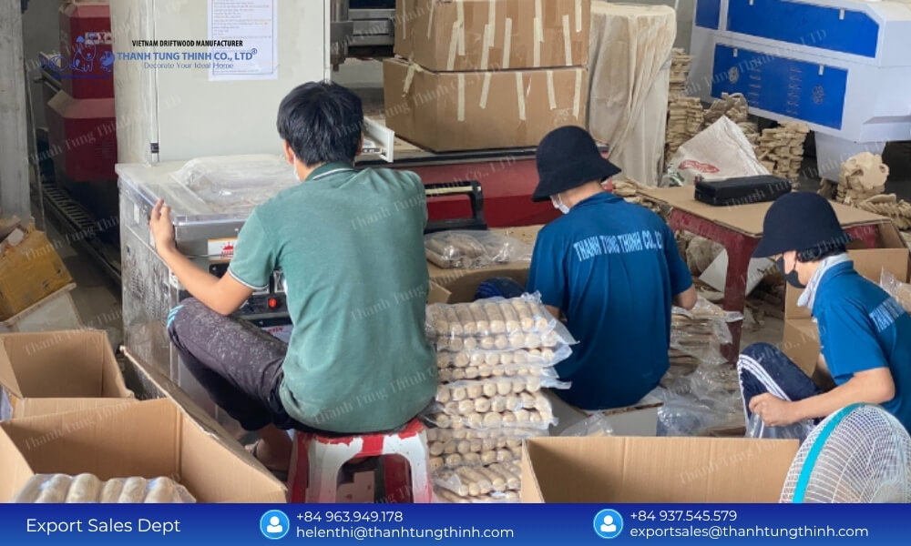 Factory operators seating at a workstation organizing plastic-wrapped pet products into stacks beside open packing boxes