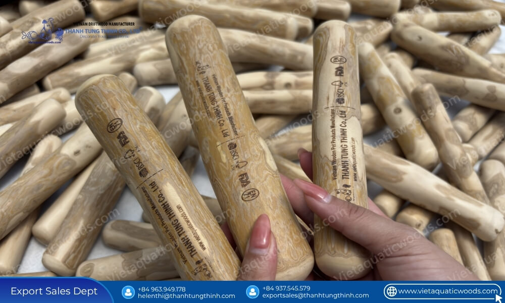 A hand holding a custom laser engraved product from a batch of bulk coffee wood chew sticks assorted sizes